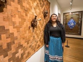 Tishara Sneed stands next to her art on exhibit, a woven design with traditional masks